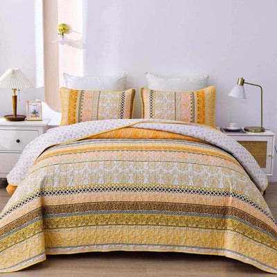 A colorful floral patterned cotton bedspread set on a bed, with a variety of matching and contrasting pillows, in a room with wooden furniture and a lamp.