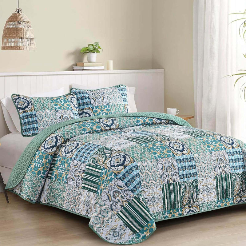A colorful floral patterned cotton bedspread set on a bed, with a variety of matching and contrasting pillows, in a room with wooden furniture and a lamp.