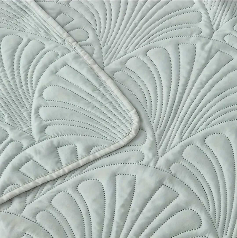 Mint green textured bedding set on a bed with pillows and a blanket, against a gray paneled wall.