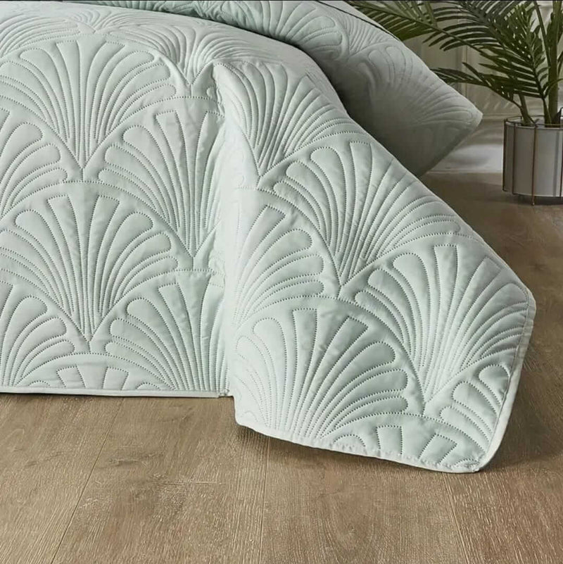 Mint green textured bedding set on a bed with pillows and a blanket, against a gray paneled wall.