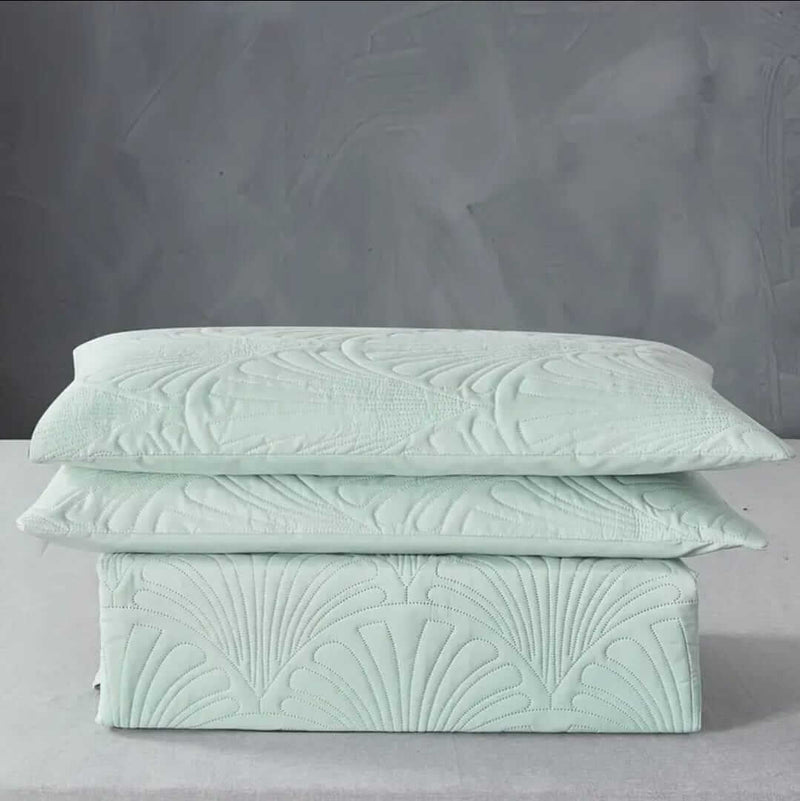 Mint green textured bedding set on a bed with pillows and a blanket, against a gray paneled wall.