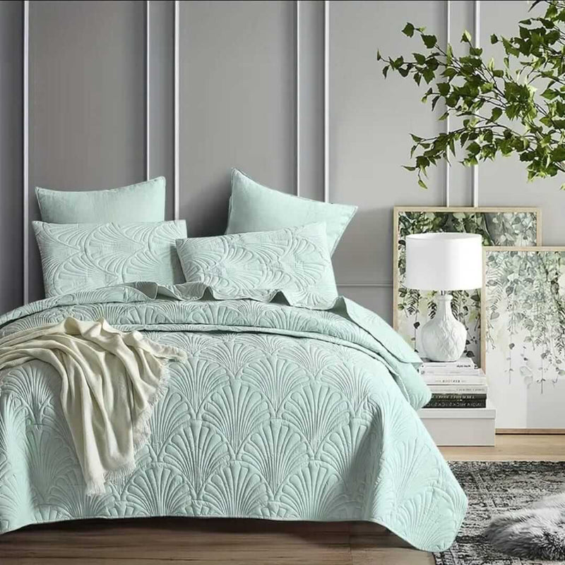 Mint green textured bedding set on a bed with pillows and a blanket, against a gray paneled wall.