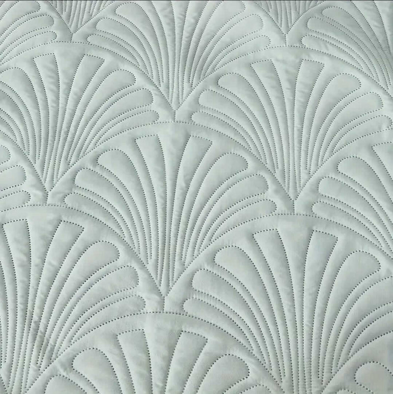 Mint green textured bedding set on a bed with pillows and a blanket, against a gray paneled wall.