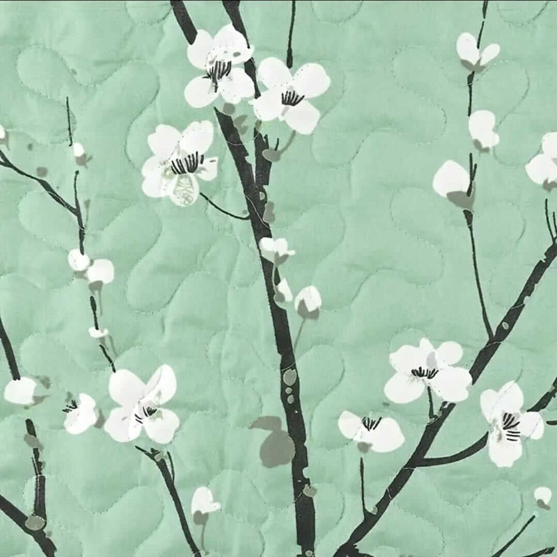 A colorful floral patterned cotton bedspread set on a bed, with a variety of matching and contrasting pillows, in a room with wooden furniture and a lamp.