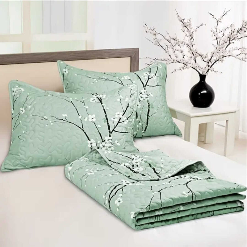 A colorful floral patterned cotton bedspread set on a bed, with a variety of matching and contrasting pillows, in a room with wooden furniture and a lamp.