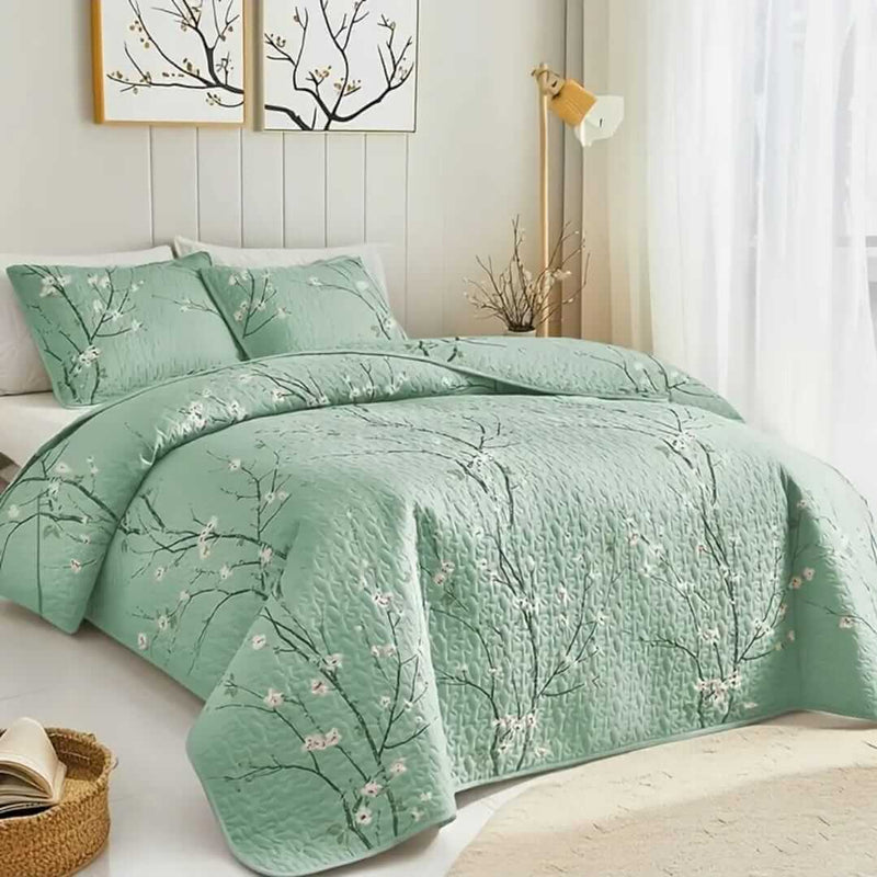 A colorful floral patterned cotton bedspread set on a bed, with a variety of matching and contrasting pillows, in a room with wooden furniture and a lamp.