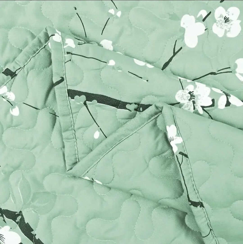 A colorful floral patterned cotton bedspread set on a bed, with a variety of matching and contrasting pillows, in a room with wooden furniture and a lamp.