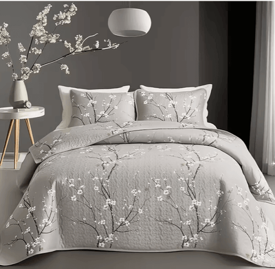 A colorful floral patterned cotton bedspread set on a bed, with a variety of matching and contrasting pillows, in a room with wooden furniture and a lamp.