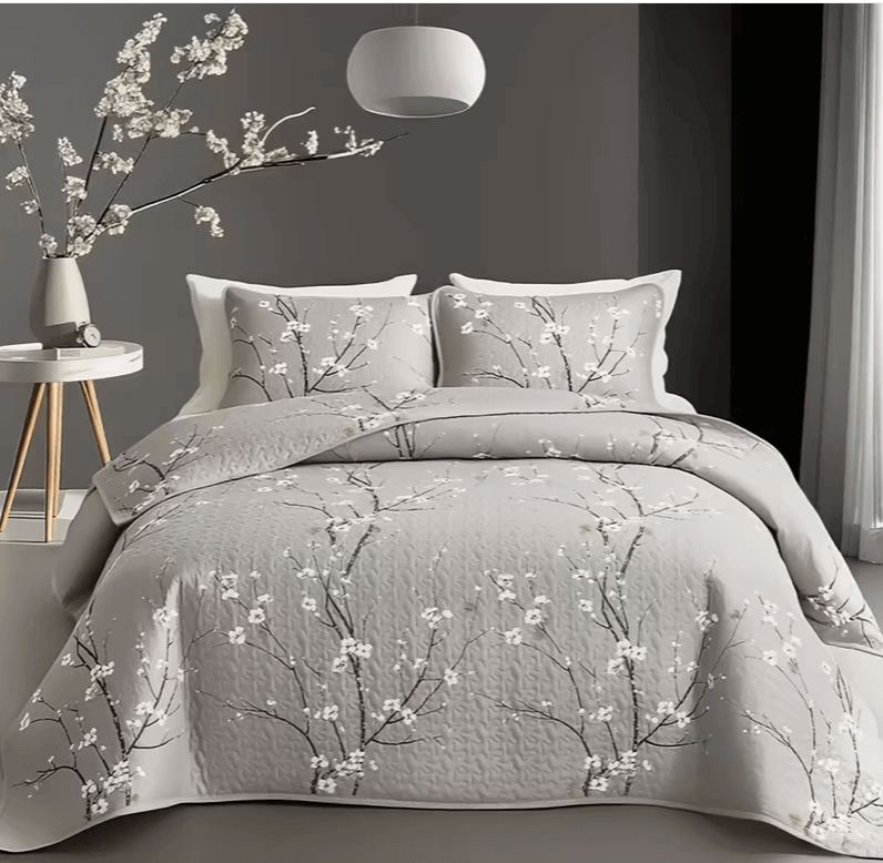 A colorful floral patterned cotton bedspread set on a bed, with a variety of matching and contrasting pillows, in a room with wooden furniture and a lamp.