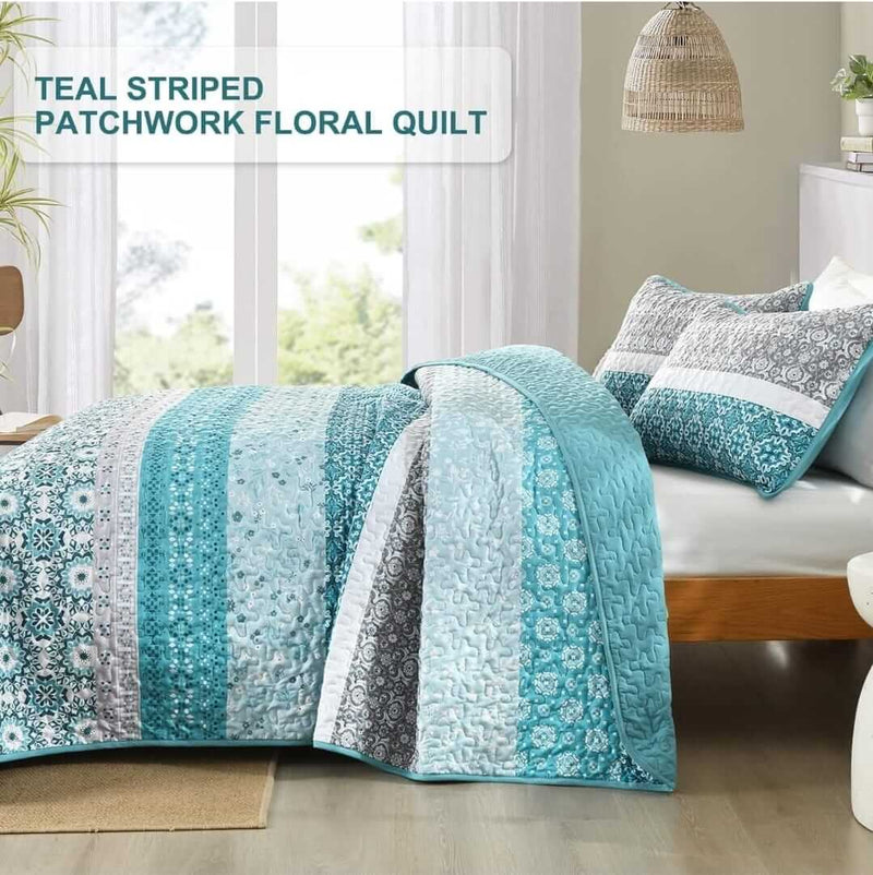 Bed with blue and gray patterned quilt and pillows in a room with a lamp and plant.