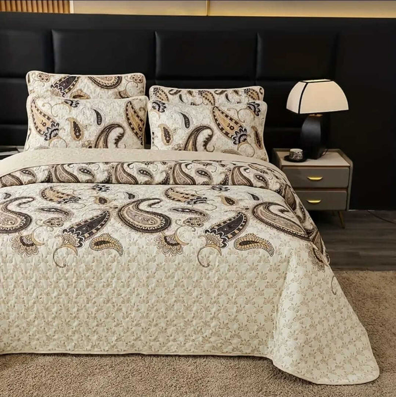 A colorful floral patterned cotton bedspread set on a bed, with a variety of matching and contrasting pillows, in a room with wooden furniture and a lamp.