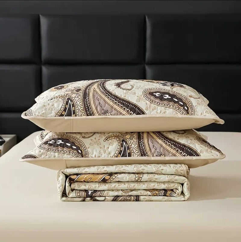 A colorful floral patterned cotton bedspread set on a bed, with a variety of matching and contrasting pillows, in a room with wooden furniture and a lamp.