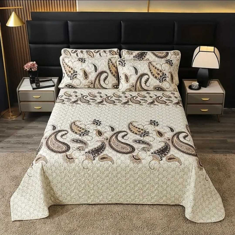 A colorful floral patterned cotton bedspread set on a bed, with a variety of matching and contrasting pillows, in a room with wooden furniture and a lamp.