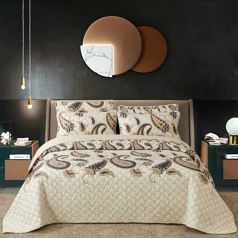 A colorful floral patterned cotton bedspread set on a bed, with a variety of matching and contrasting pillows, in a room with wooden furniture and a lamp.