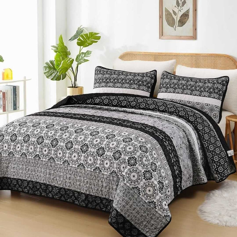 A colorful floral patterned cotton bedspread set on a bed, with a variety of matching and contrasting pillows, in a room with wooden furniture and a lamp.