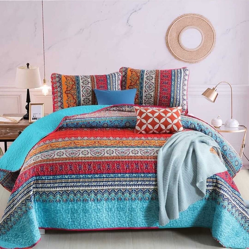 Colorful patterned bedding set on a bed in a room with a lamp and nightstand.