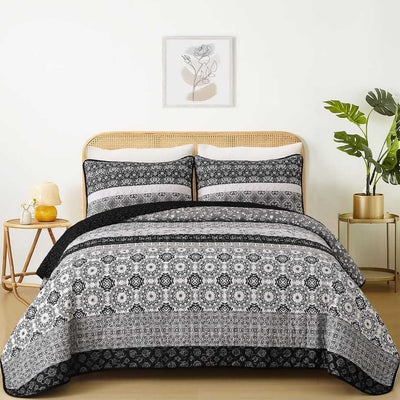A colorful floral patterned cotton bedspread set on a bed, with a variety of matching and contrasting pillows, in a room with wooden furniture and a lamp.