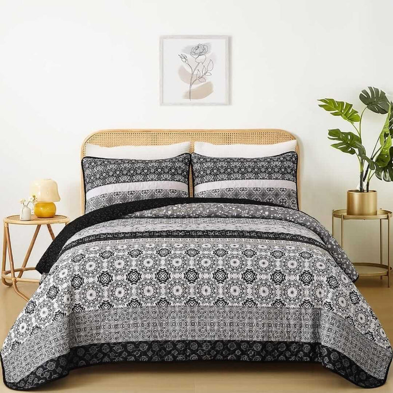 A colorful floral patterned cotton bedspread set on a bed, with a variety of matching and contrasting pillows, in a room with wooden furniture and a lamp.