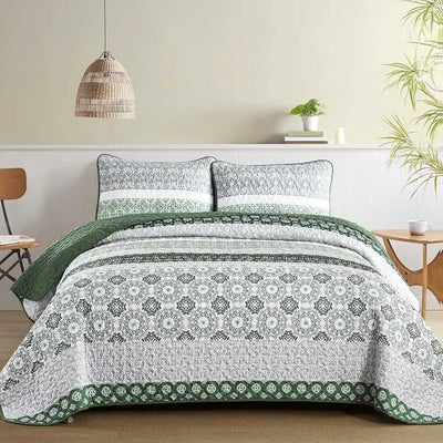A colorful floral patterned cotton bedspread set on a bed, with a variety of matching and contrasting pillows, in a room with wooden furniture and a lamp.