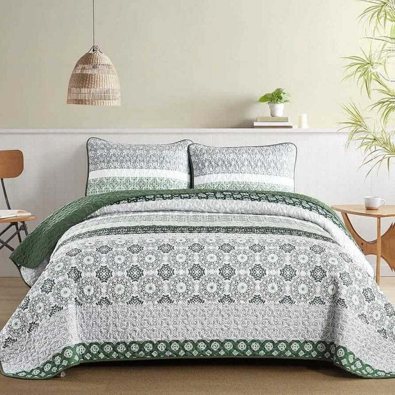 A colorful floral patterned cotton bedspread set on a bed, with a variety of matching and contrasting pillows, in a room with wooden furniture and a lamp.