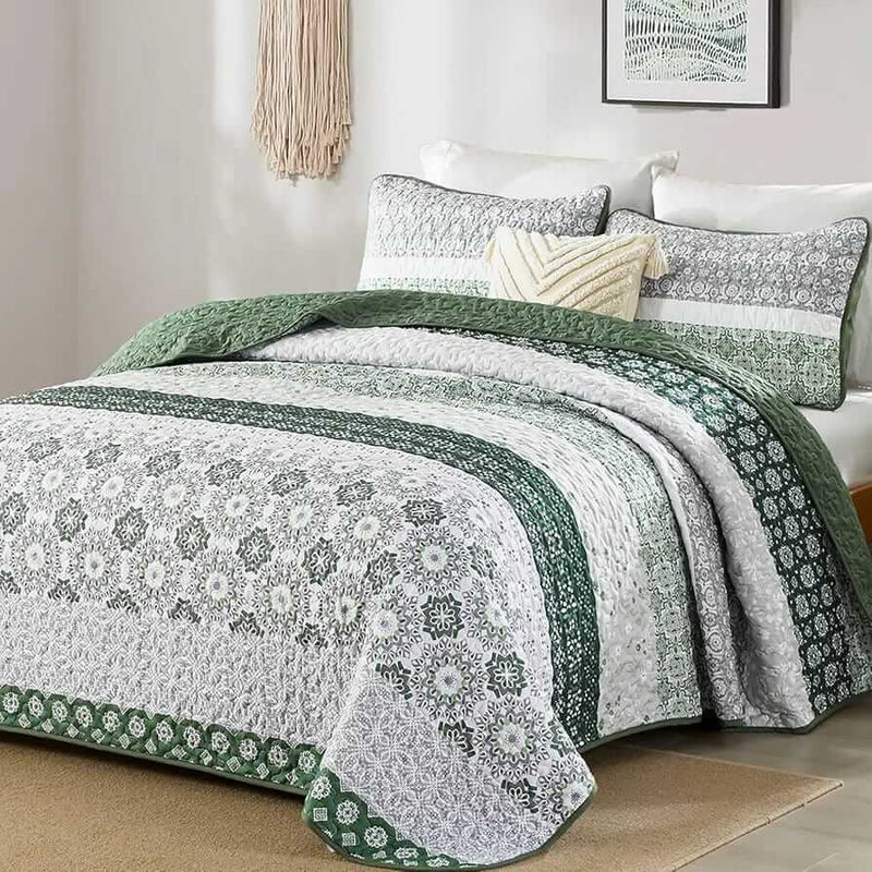 A colorful floral patterned cotton bedspread set on a bed, with a variety of matching and contrasting pillows, in a room with wooden furniture and a lamp.