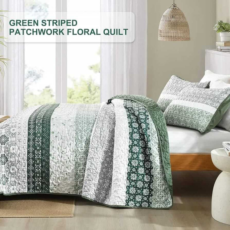 A colorful floral patterned cotton bedspread set on a bed, with a variety of matching and contrasting pillows, in a room with wooden furniture and a lamp.