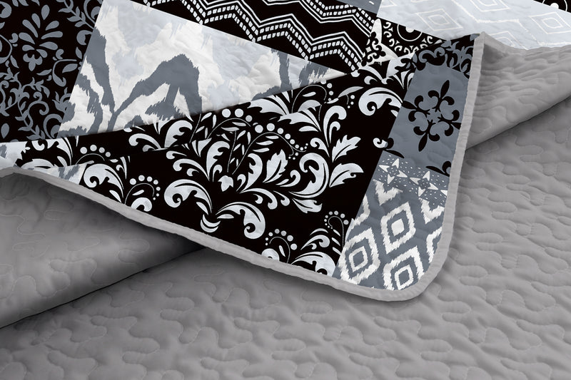 Patterned quilt with black, white, and gray designs on a textured surface.