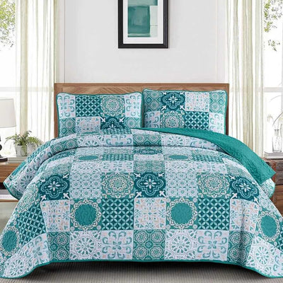 A colorful floral patterned cotton bedspread set on a bed, with a variety of matching and contrasting pillows, in a room with wooden furniture and a lamp.