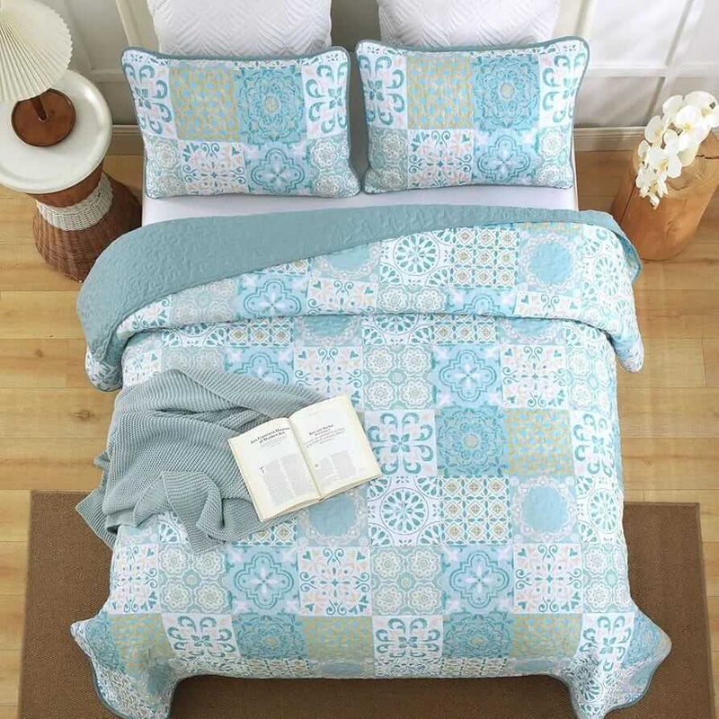 Blue and green patchwork quilt set on a bed in a bedroom.