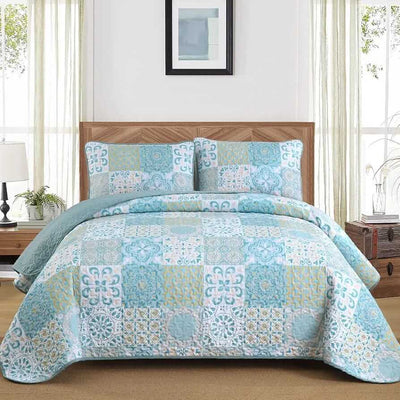 Blue and green patchwork quilt set on a bed in a bedroom.