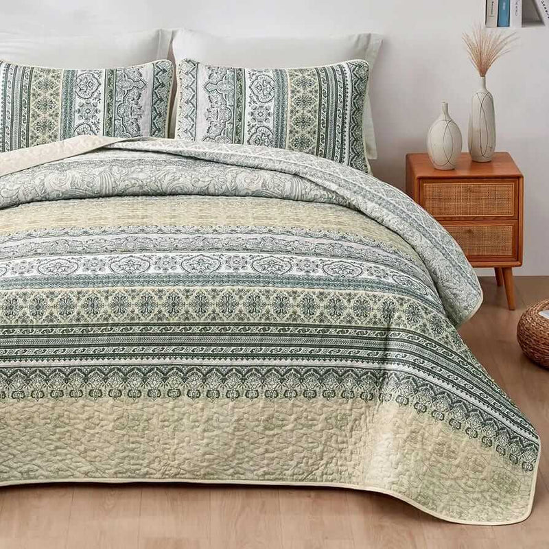 Patterned quilt set on a bed in a bedroom with a nightstand and plant.
