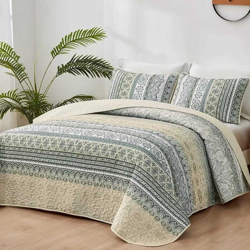 Patterned quilt set on a bed in a bedroom with a nightstand and plant.
