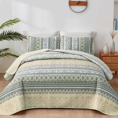Patterned quilt set on a bed in a bedroom with a nightstand and plant.