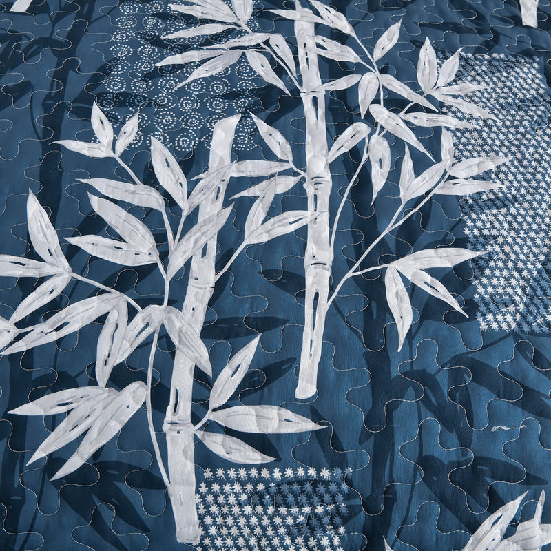 Blue and white leaf-patterned comforter set on a bed in a bedroom.