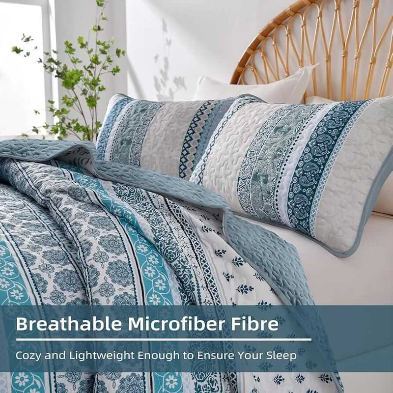 Patterned quilt set on a bed in a bedroom with a nightstand and plant.