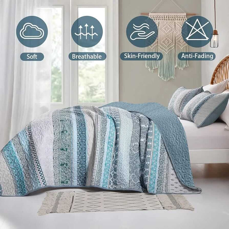 Patterned quilt set on a bed in a bedroom with a nightstand and plant.