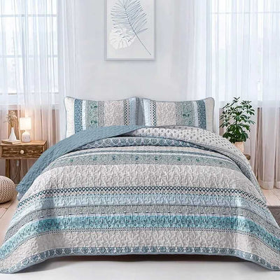Patterned quilt set on a bed in a bedroom with a nightstand and plant.