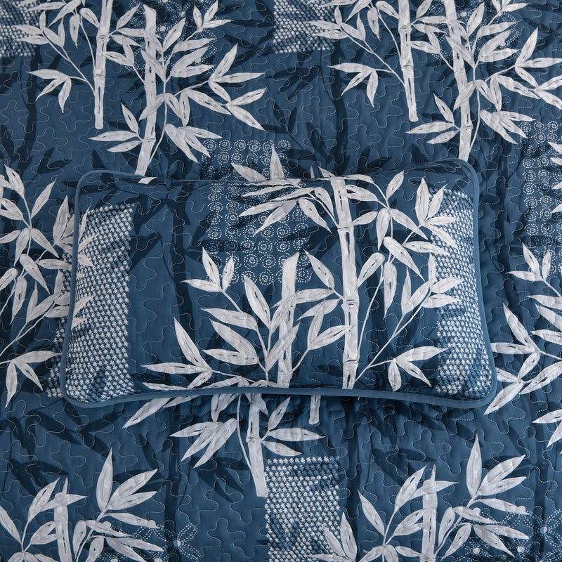 Blue and white leaf-patterned comforter set on a bed in a bedroom.