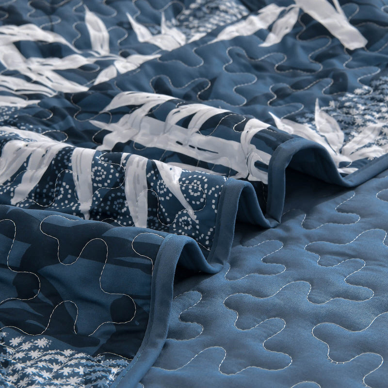 Blue and white leaf-patterned comforter set on a bed in a bedroom.