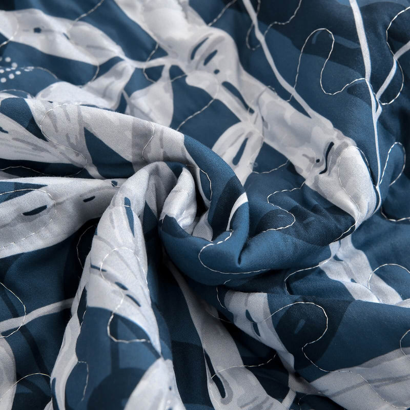 Blue and white leaf-patterned comforter set on a bed in a bedroom.