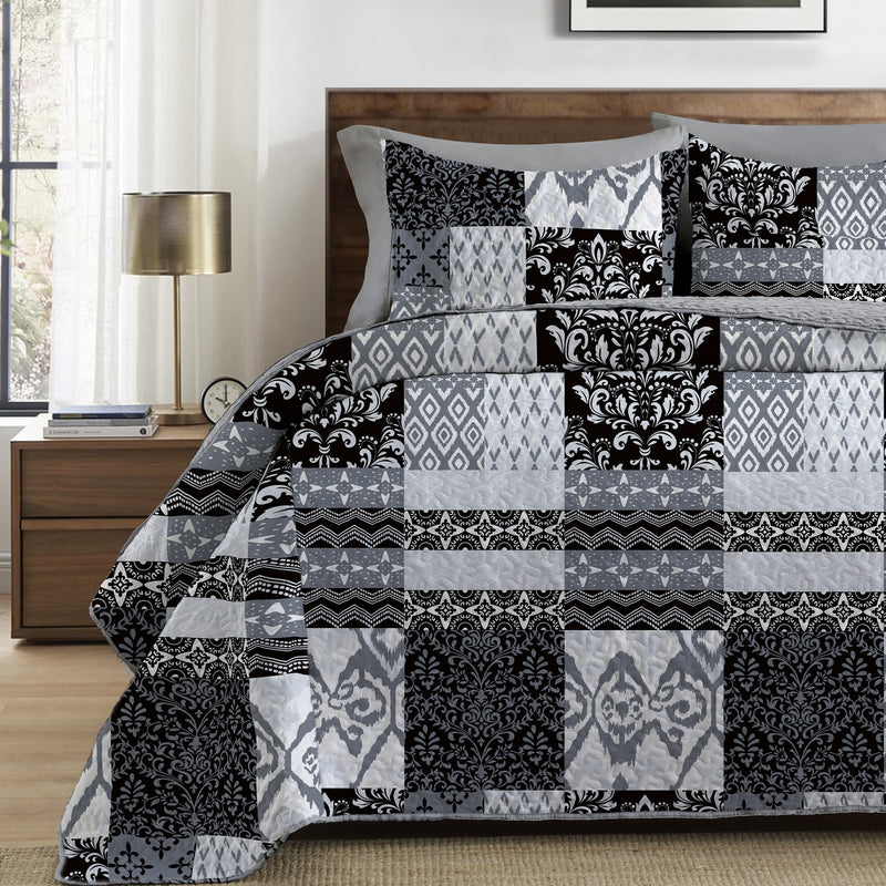 Patchwork quilt with black, gray, and white patterns on a bed in a bedroom setting.