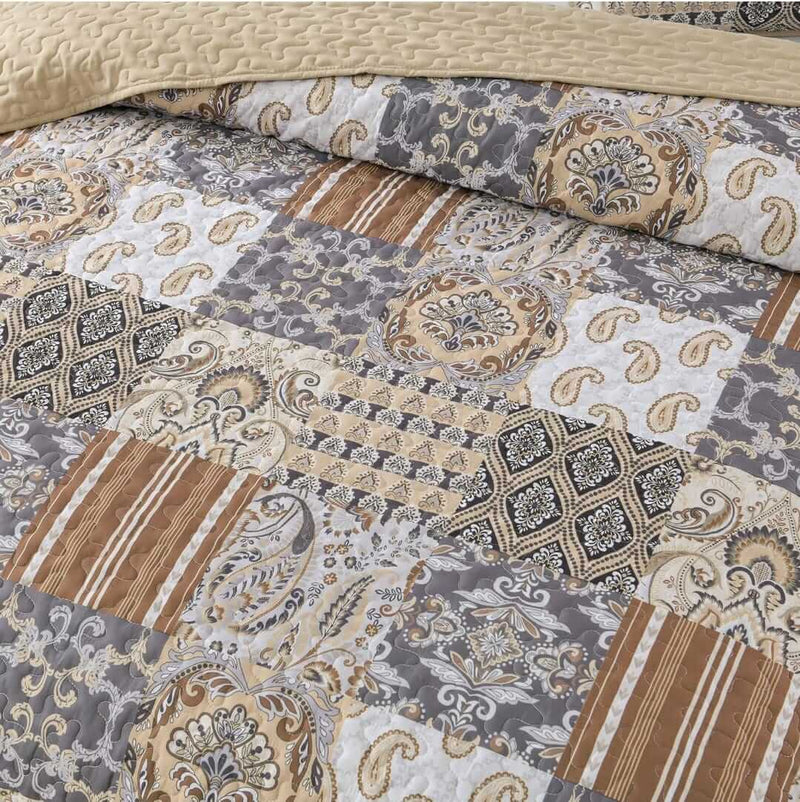 A colorful floral patterned cotton bedspread set on a bed, with a variety of matching and contrasting pillows, in a room with wooden furniture and a lamp.