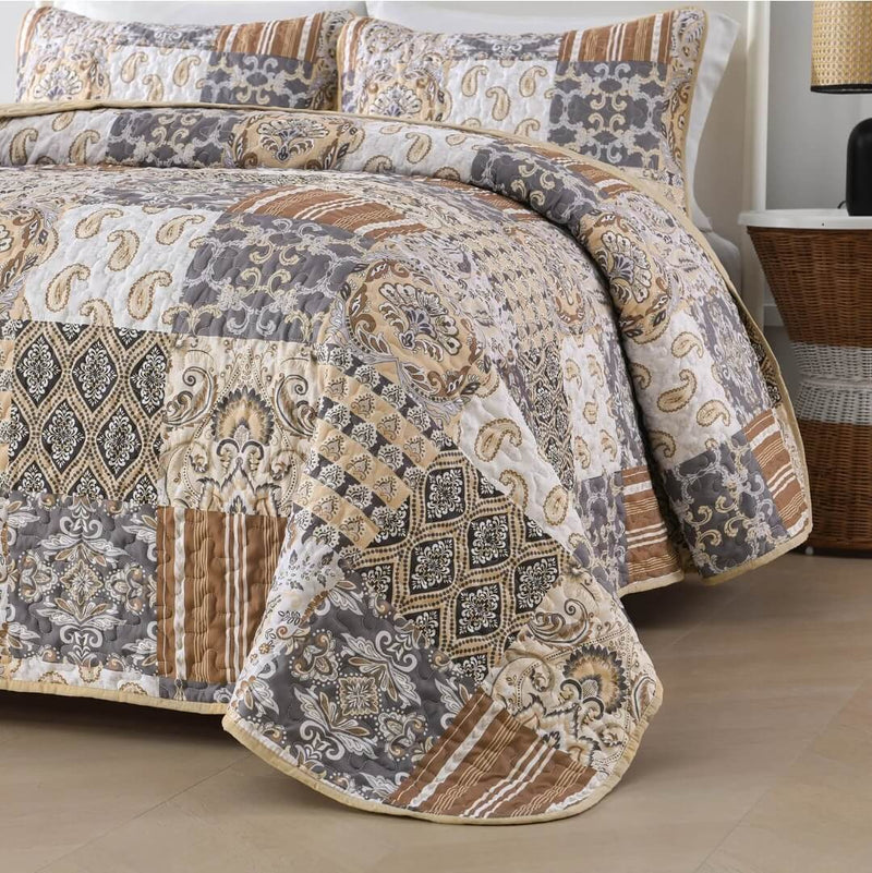 A colorful floral patterned cotton bedspread set on a bed, with a variety of matching and contrasting pillows, in a room with wooden furniture and a lamp.