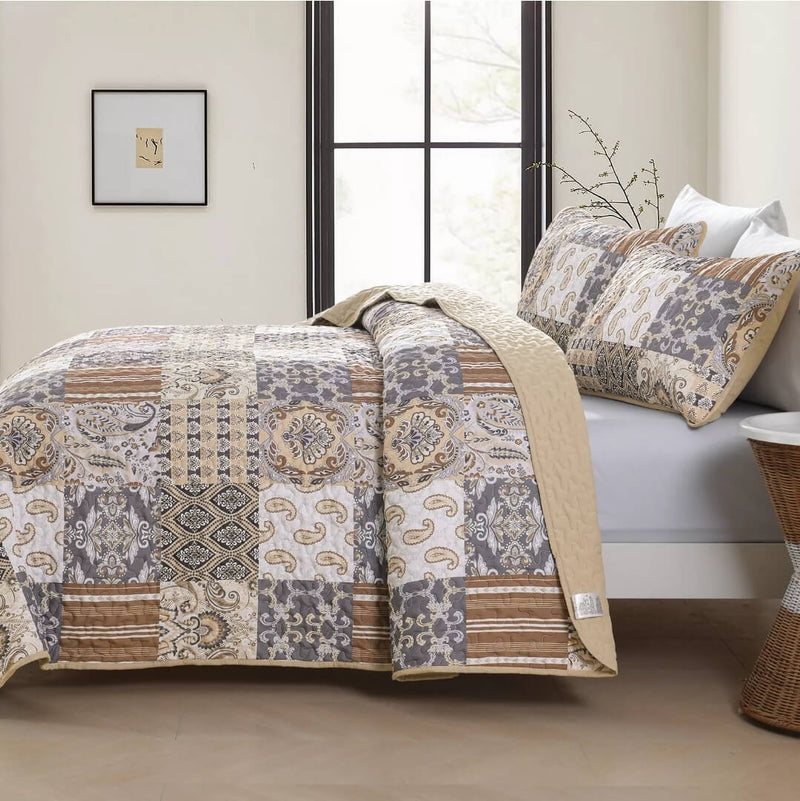 A colorful floral patterned cotton bedspread set on a bed, with a variety of matching and contrasting pillows, in a room with wooden furniture and a lamp.