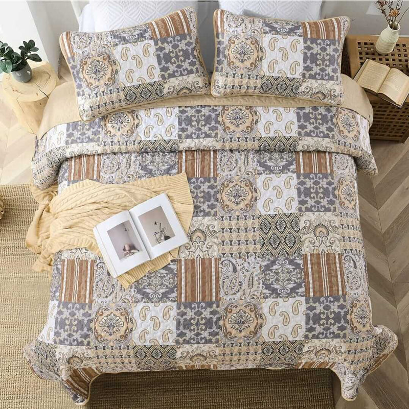 A colorful floral patterned cotton bedspread set on a bed, with a variety of matching and contrasting pillows, in a room with wooden furniture and a lamp.