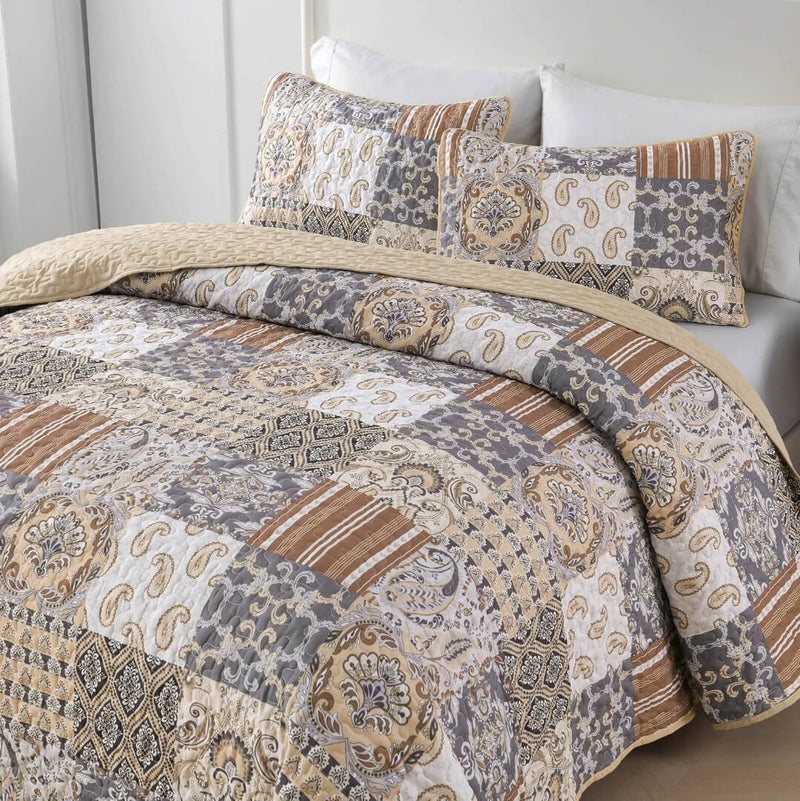 A colorful floral patterned cotton bedspread set on a bed, with a variety of matching and contrasting pillows, in a room with wooden furniture and a lamp.