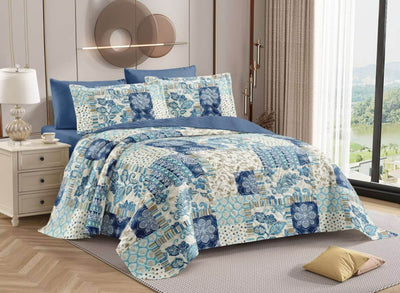 Blue and white floral quilt set on a bed in a bedroom with a lamp and window in the background.