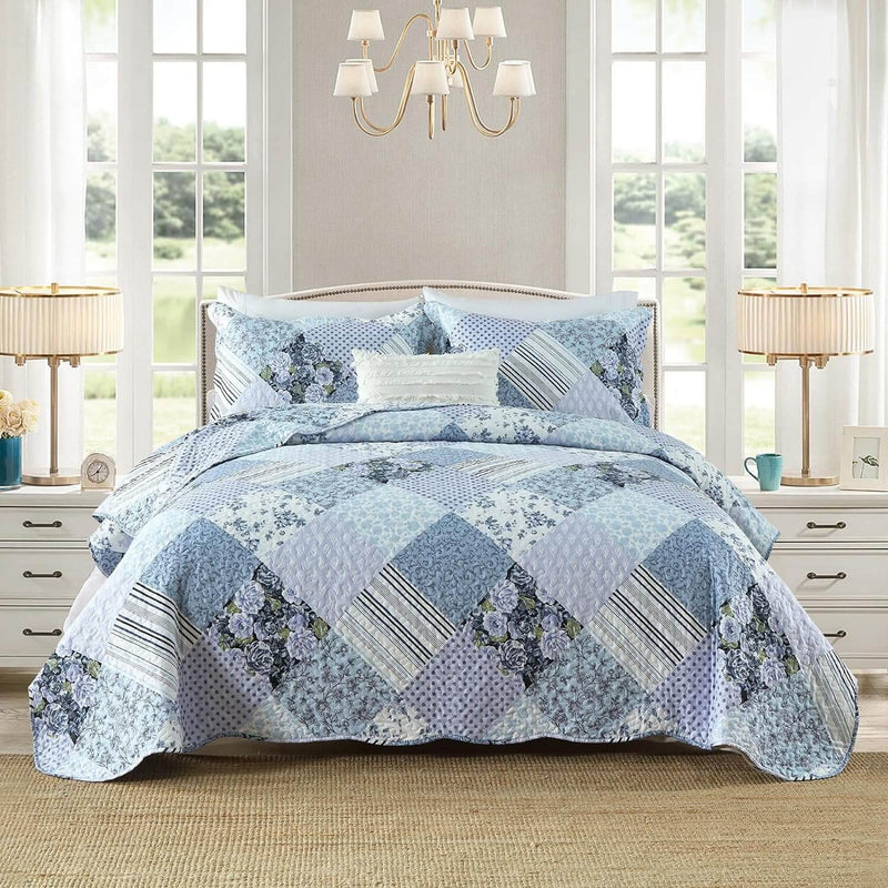 Blue patchwork quilt set on a bed in a bedroom with lamps and a chandelier.