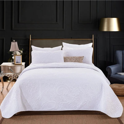 White quilted coverlet on a bed with matching pillows in a bedroom setting.